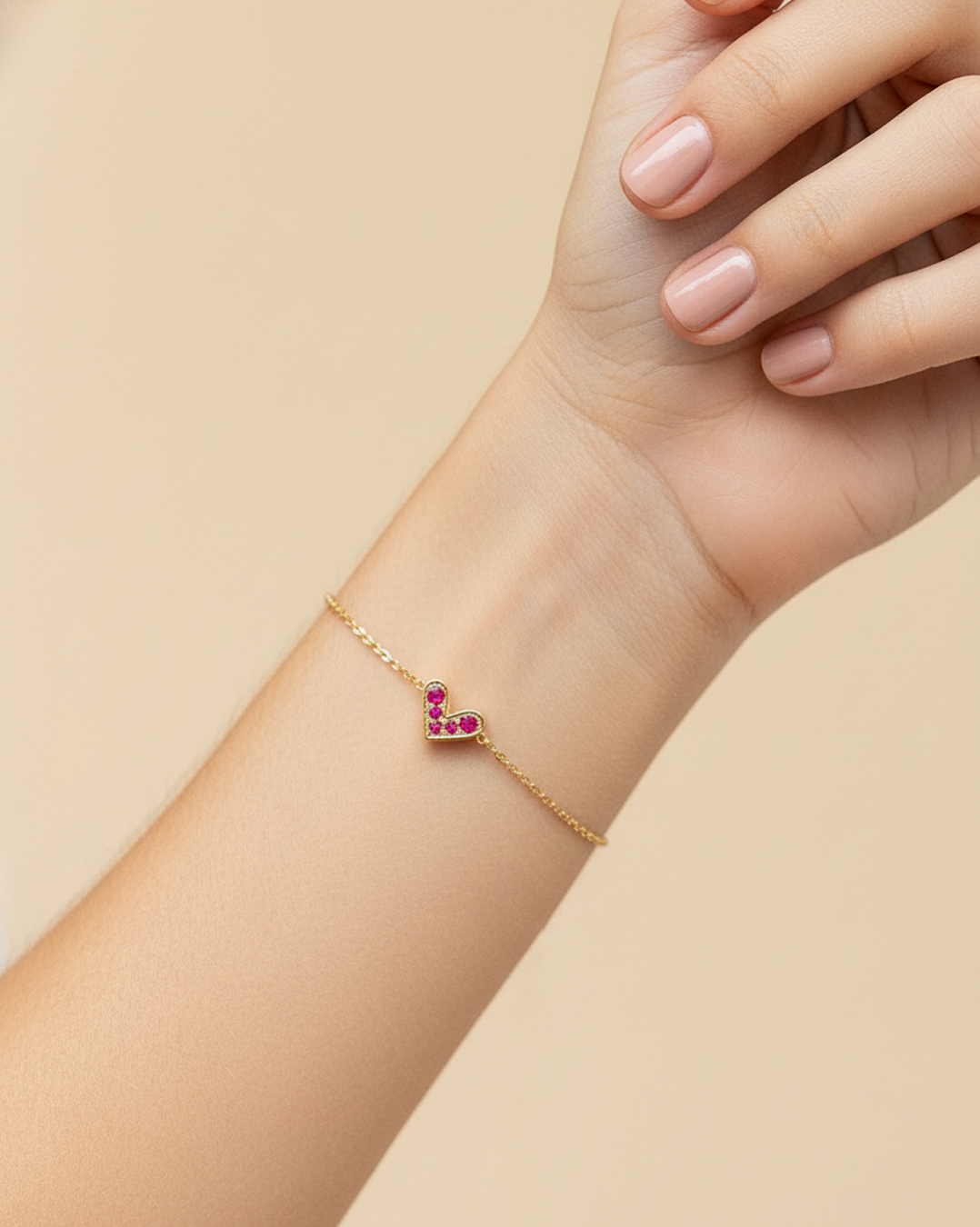 Gold-plated stainless steel bracelet with fuchsia crystal heart charm on wrist against beige background.