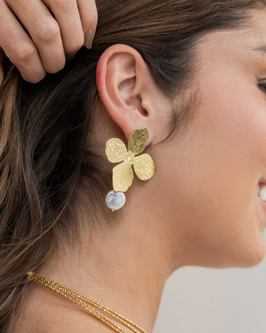 Pair of gold floral earrings with white charm drops on champagne satin background.