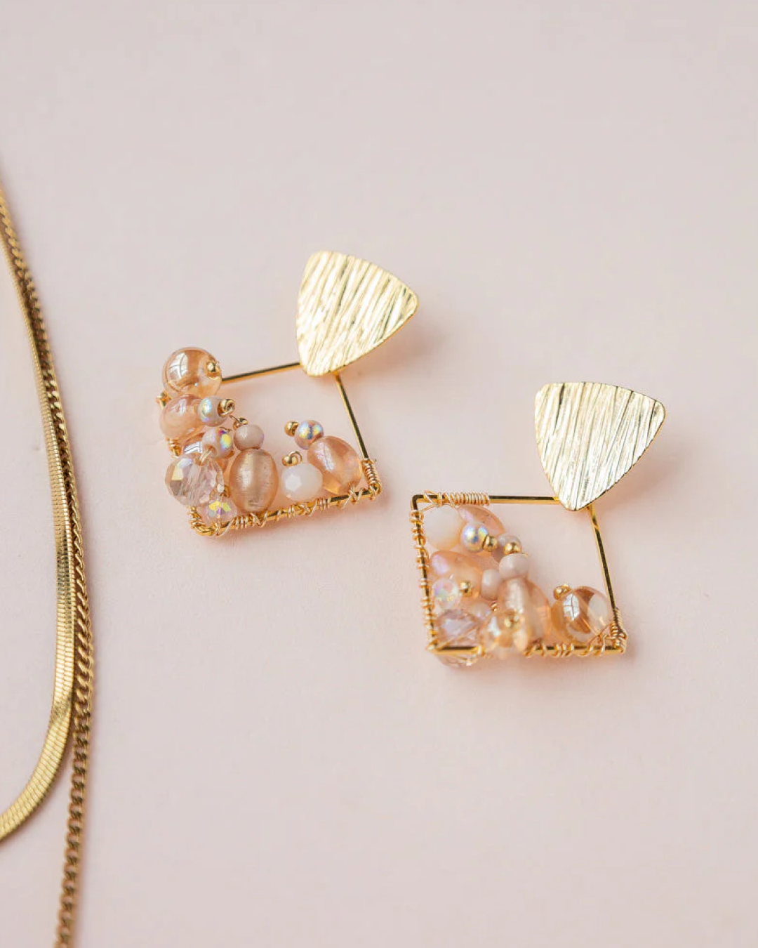 Pair of gold diamond-shaped beaded earrings with Czech seed beads, Murano and glass on light lilac surface.