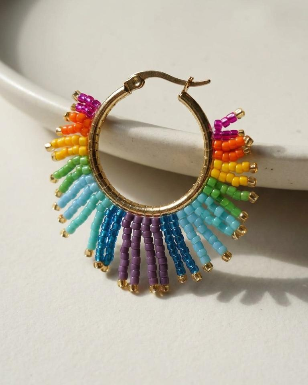 Gold hoop earring with rainbow Miyuki fringe displayed on a white tray.