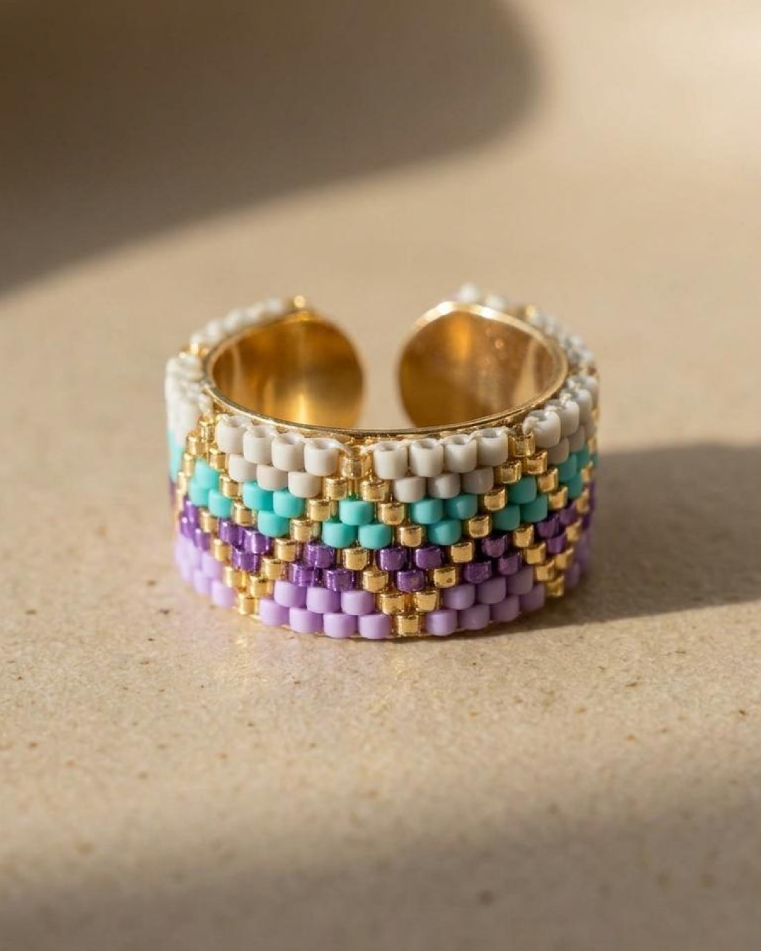 Adjustable pastel Miyuki ring displayed on a beige surface.