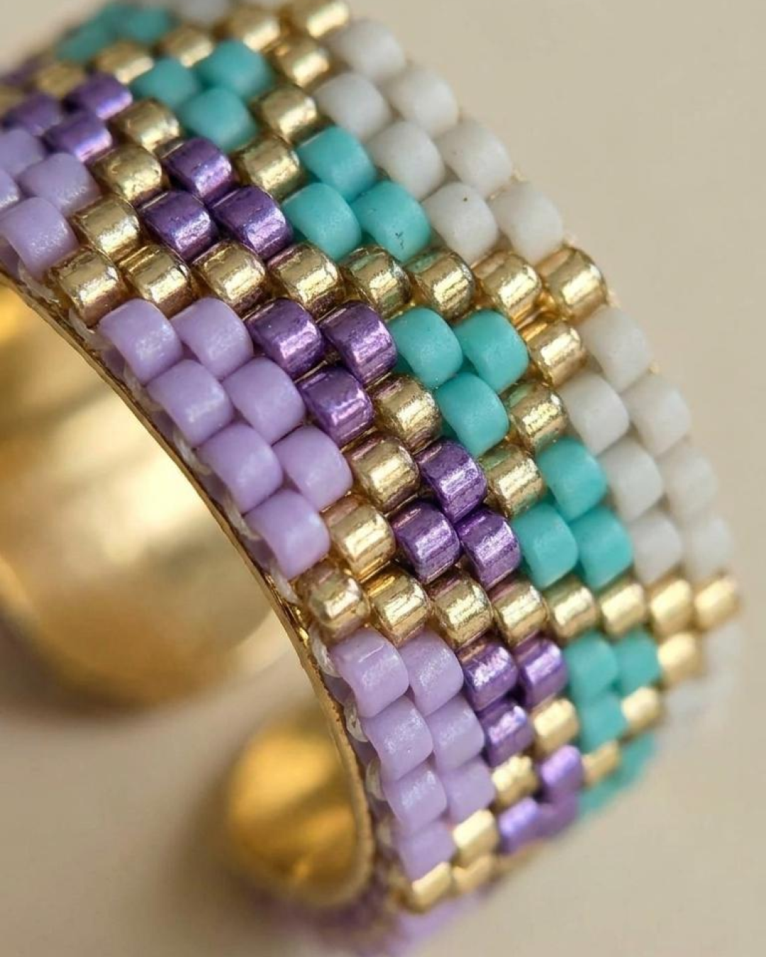 Macro detail of a Miyuki ring with a geometric pattern in lilac, aqua, white, and gold.