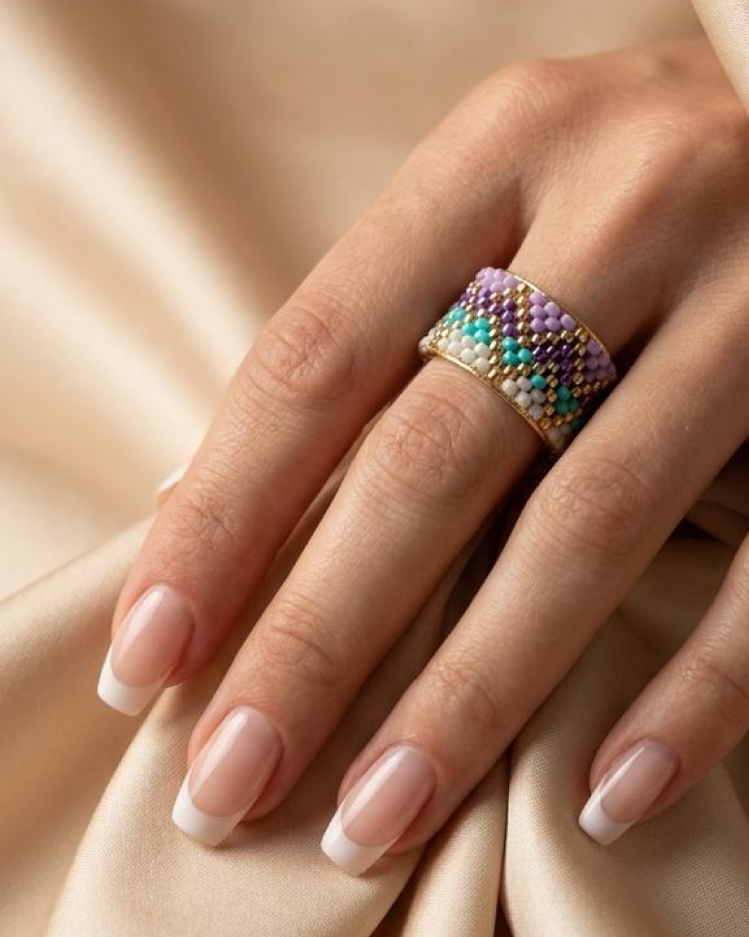 Hand with a French manicure wearing a wide multicolor woven Miyuki ring.