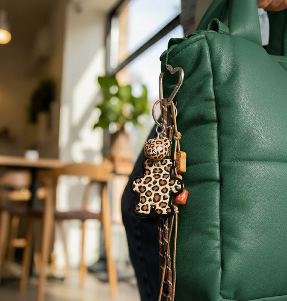 Bear bag charm with leopard print and mixed charms clipped to a handbag strap.