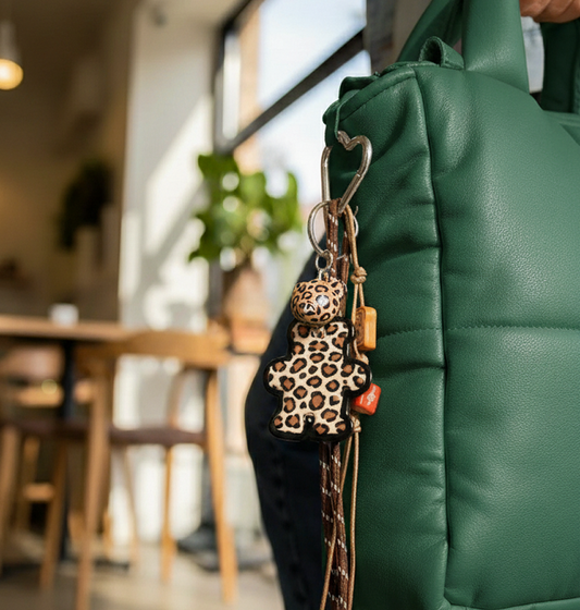 Bear bag charm with leopard print and mixed charms clipped to a handbag strap.