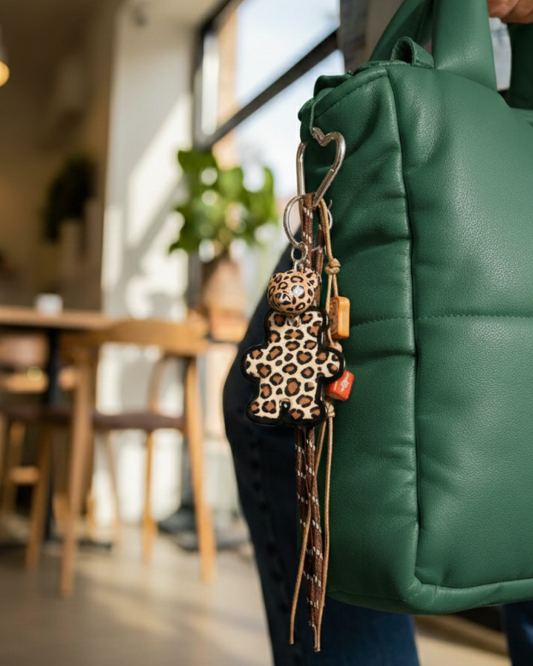 Bear bag charm with leopard print and mixed charms clipped to a handbag strap.