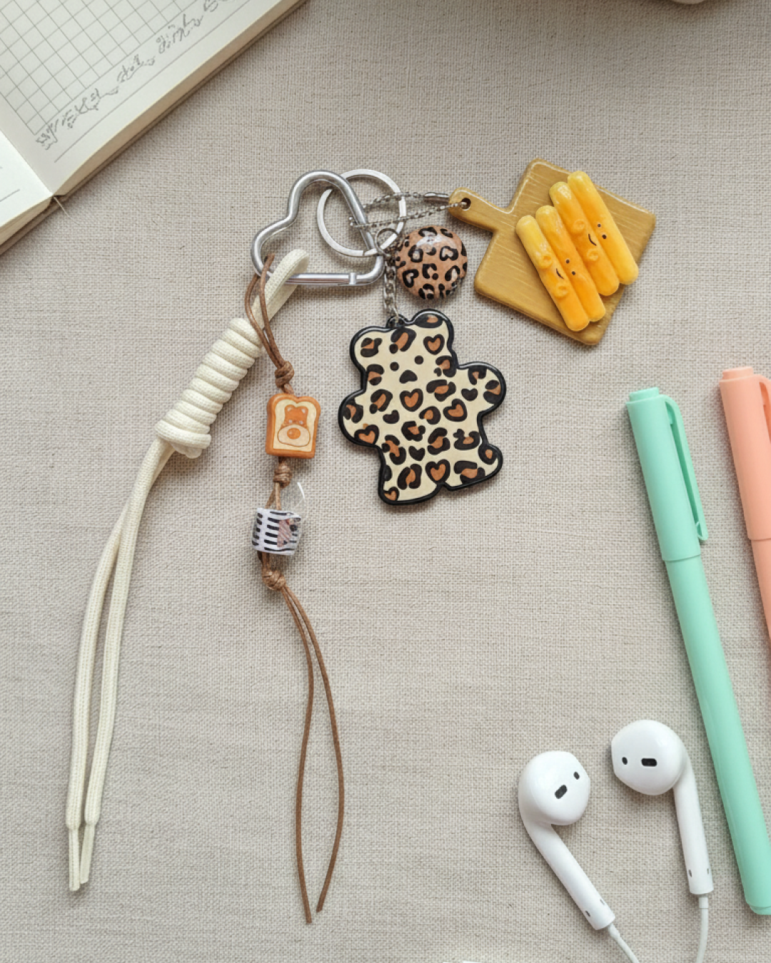 Bear bag charm with leopard print, silver cloud carabiner and mini heart charms on a neutral fabric background.