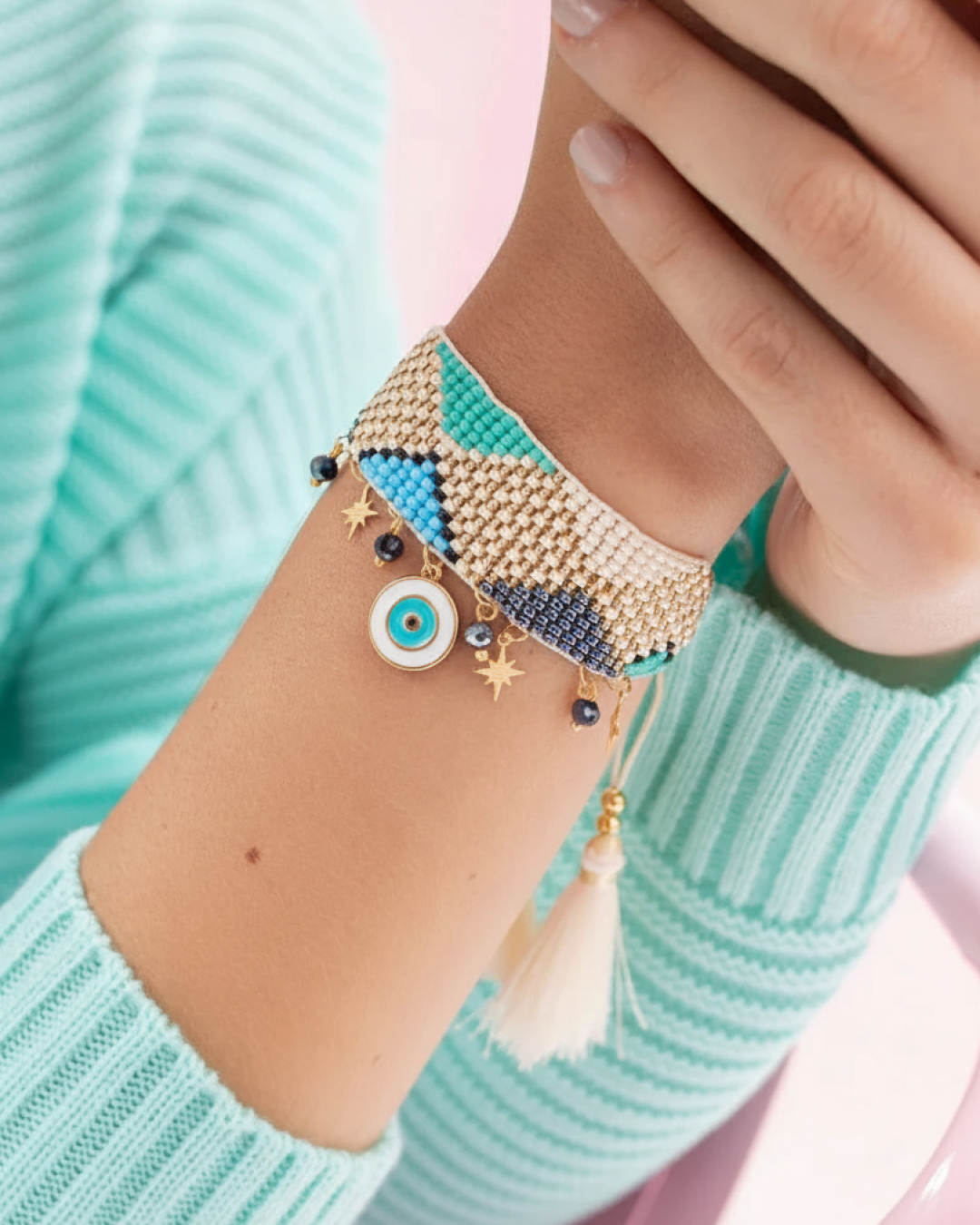 Wide woven Czech seed bead bracelet with blue evil-eye charm, gold stars, navy beads, and a cream tassel on the wrist.