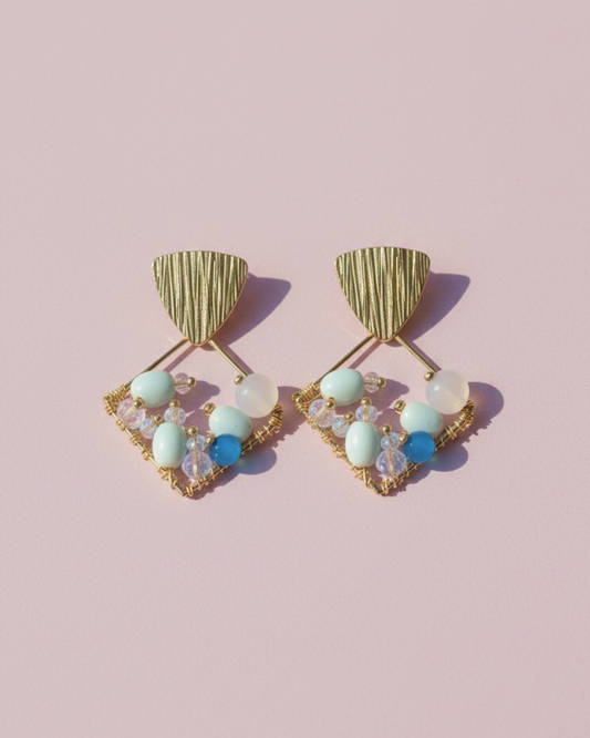 Pair of gold diamond-shaped beaded earrings with Czech seed beads, Murano and glass on light lilac surface.