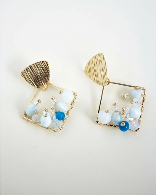 Pair of gold diamond-shaped beaded earrings with Czech seed beads, Murano and glass on light surface.