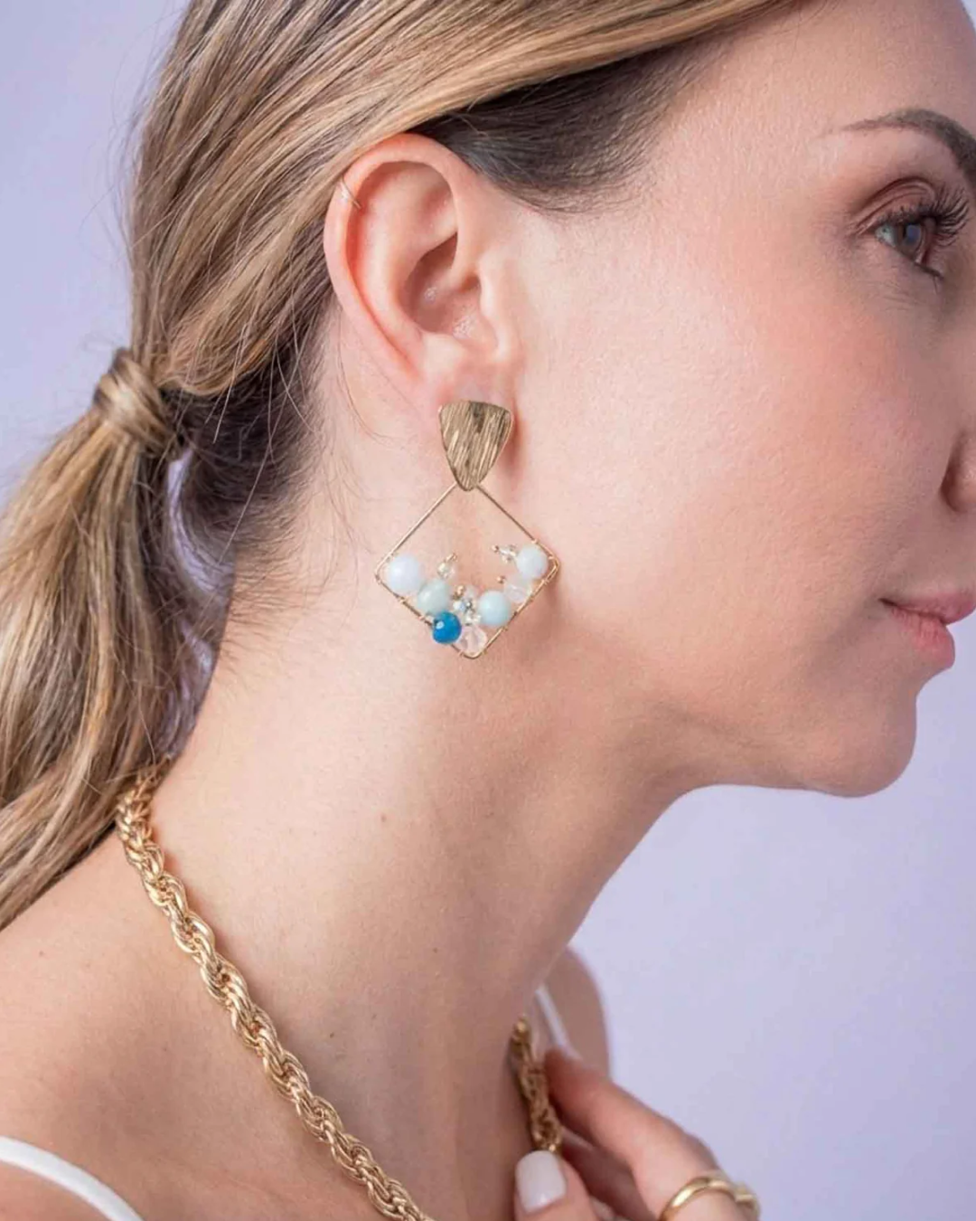 Side view of a gold geometric dangling earring with handcrafted blue and white bead details.