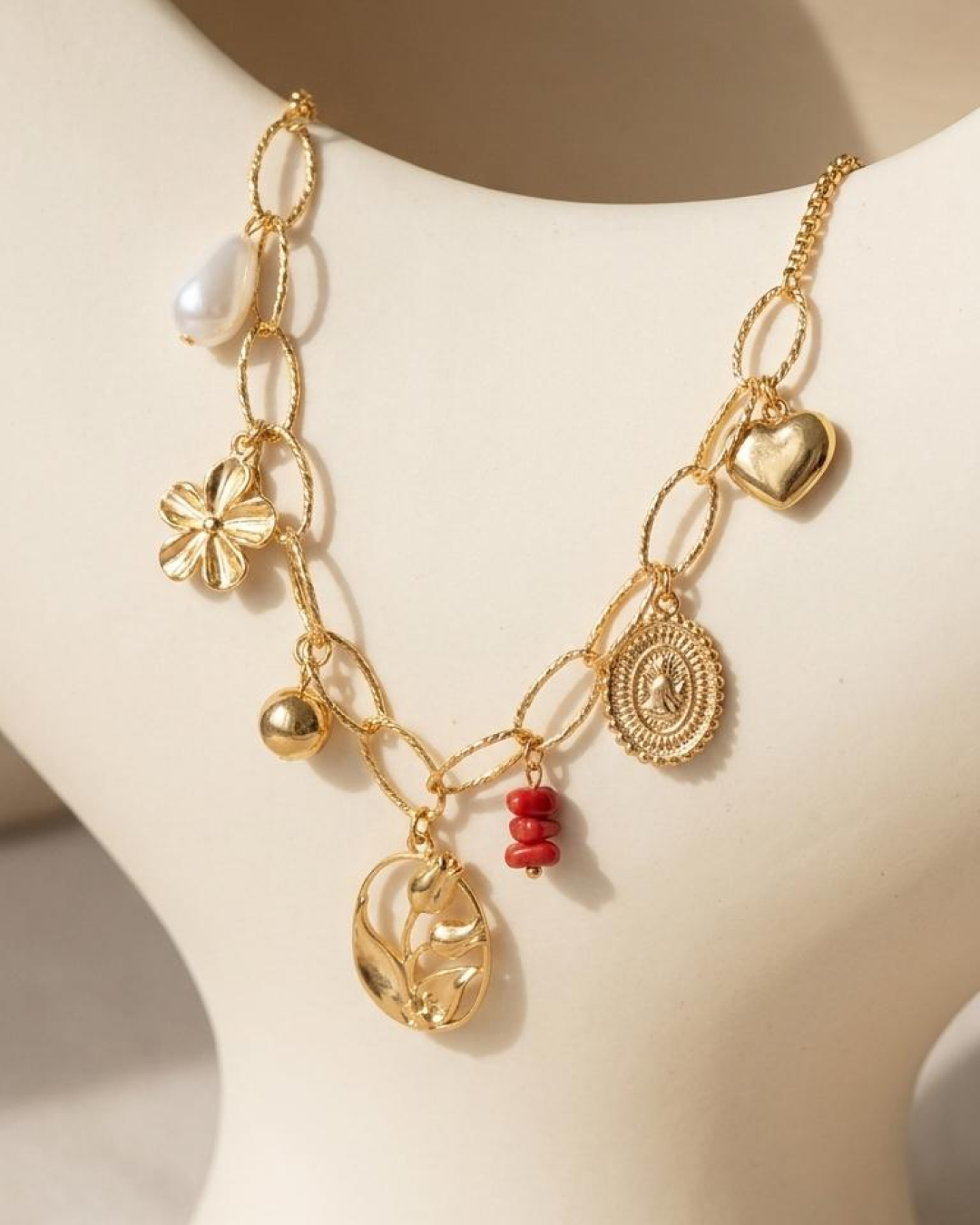 Gold multi-charm necklace displayed on a white jewelry bust.
