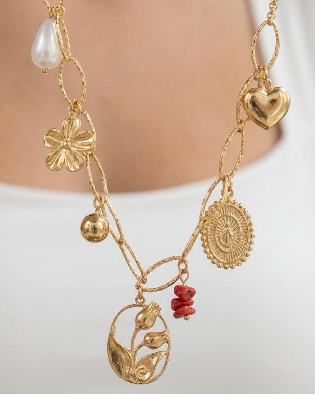 Close-up of a gold necklace with pearl-style, flower, heart, medallion, and botanical charms.