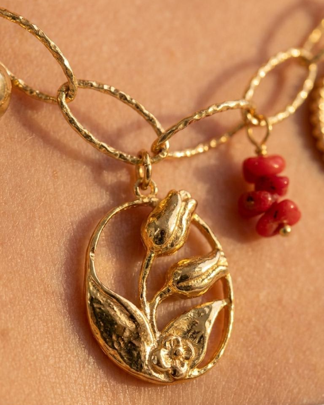 Macro detail of a gold botanical charm with a red accent on a charm necklace.