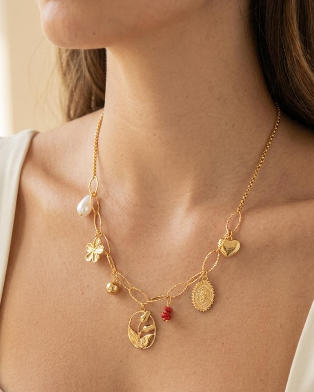 Woman wearing a gold necklace with heart, flower, medallion, and botanical charms.