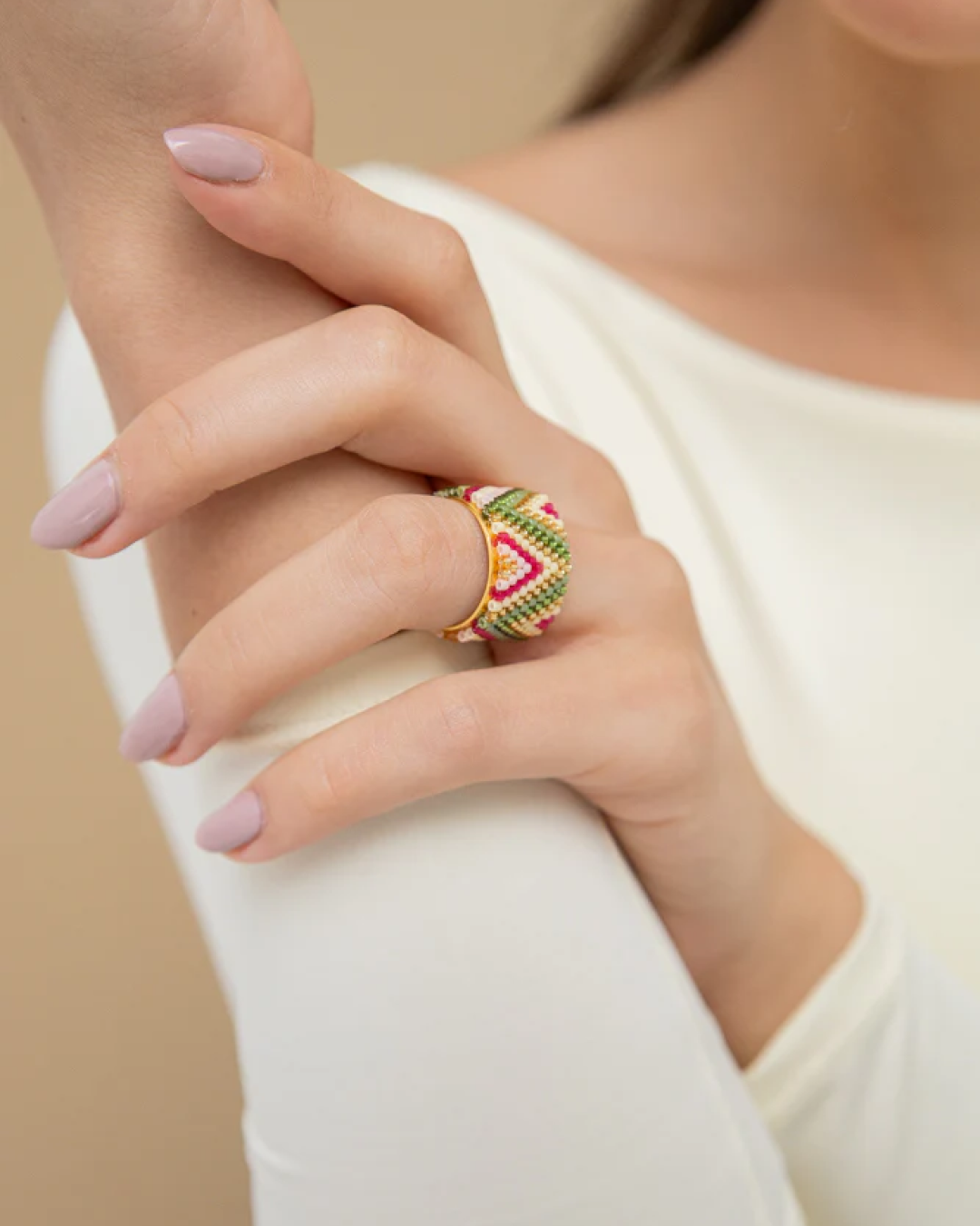 Woman’s hand wearing a wide Miyuki-beaded ring in multicolor on a gold-tone base.