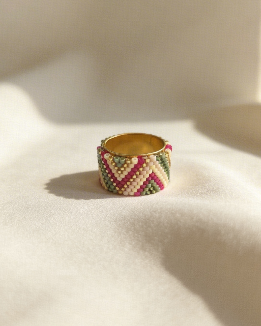 Wide-band ring with a Miyuki chevron design resting on ivory fabric.