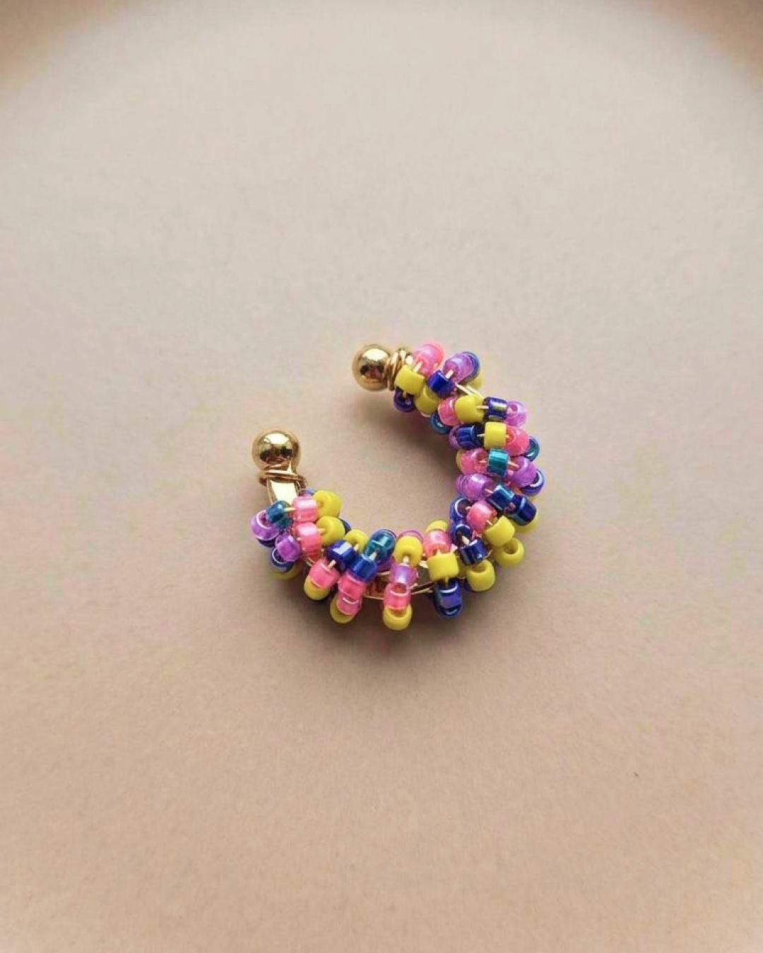 Single multicolor beaded ear cuff on a neutral background with a gold-tone open cuff base.