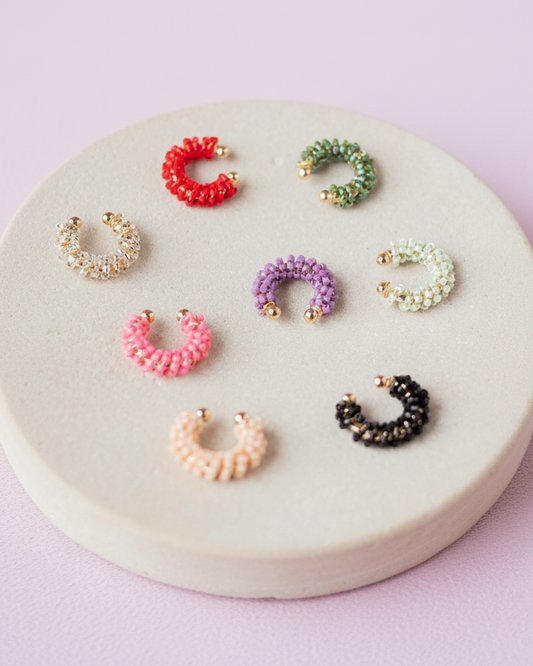 Colorful adjustable Miyuki earcuffs with gold ends arranged on a round display.