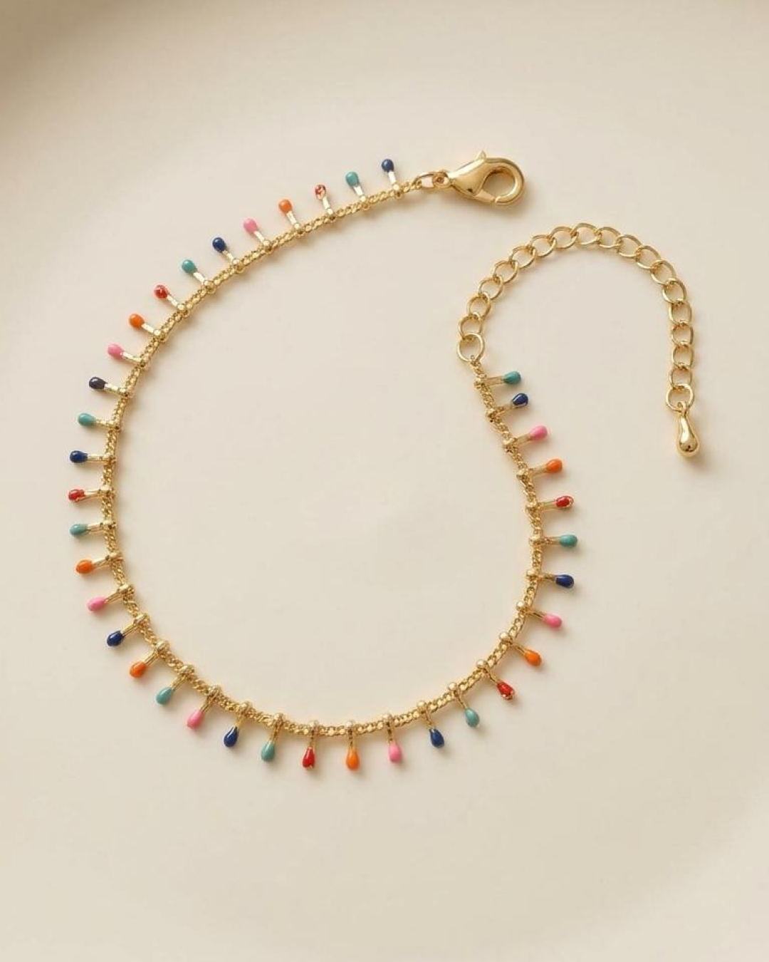 Gold anklet with multicolor drop charms laid flat on a neutral surface.