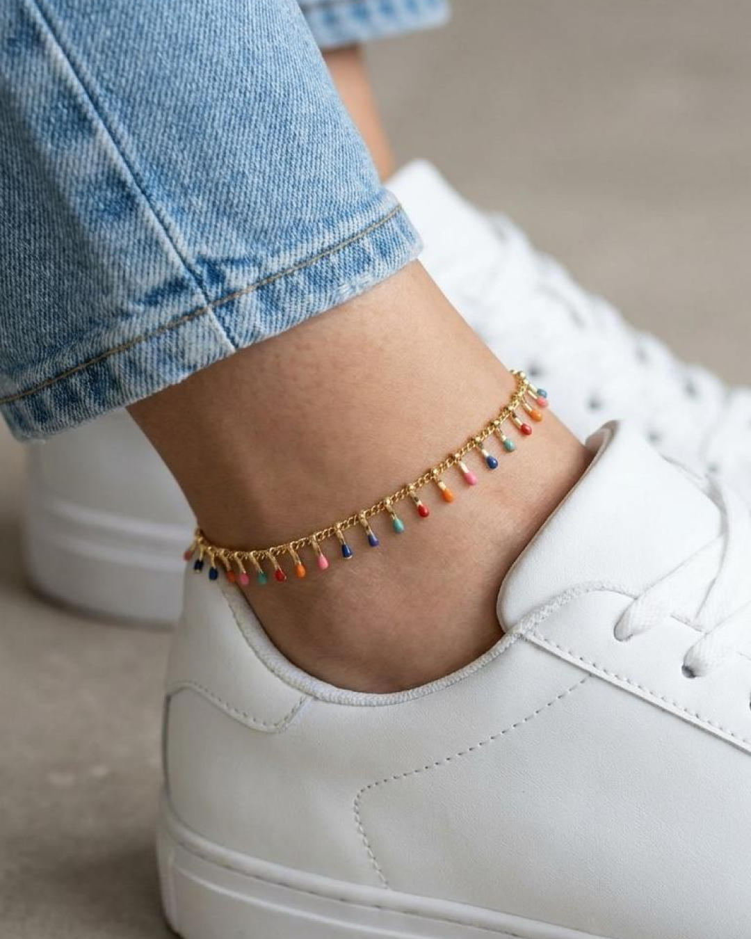 Multicolor gold anklet paired with white sneakers and light-wash jeans.
