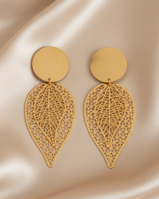 Pair of gold double-leaf filigree earrings with round tops laid on beige satin fabric.