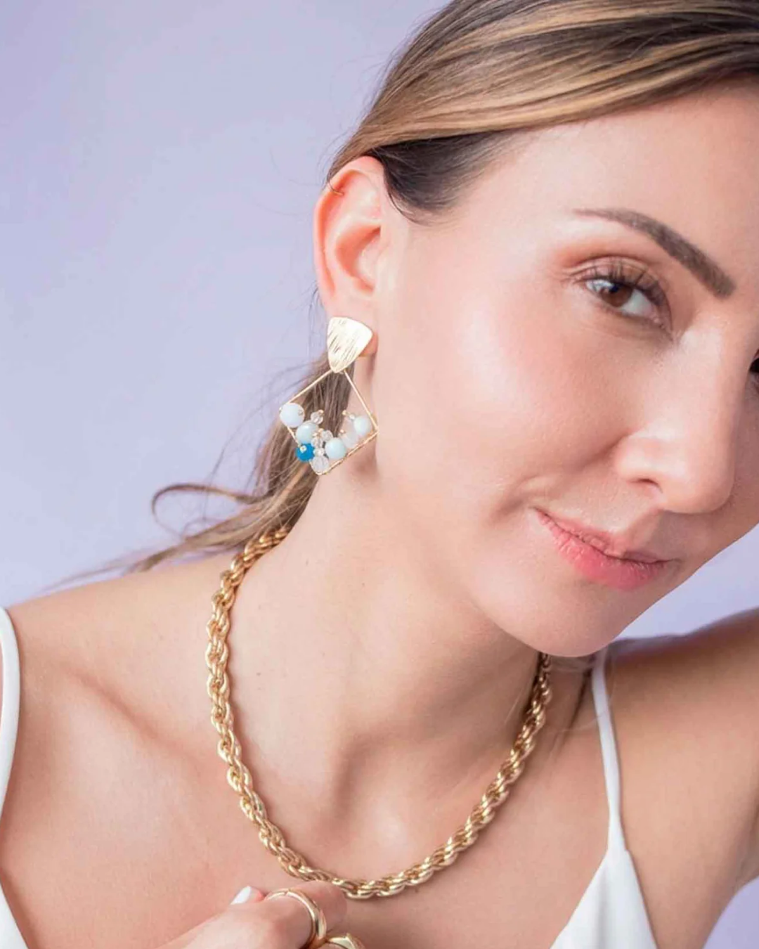 Woman wearing gold geometric drop earrings with white, soft blue, and deep blue beads.
