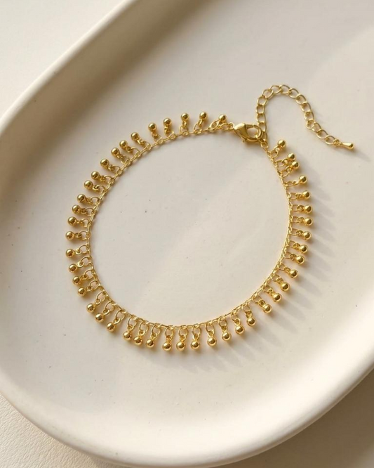 Gold anklet with tiny sphere charms displayed flat on a white tray.