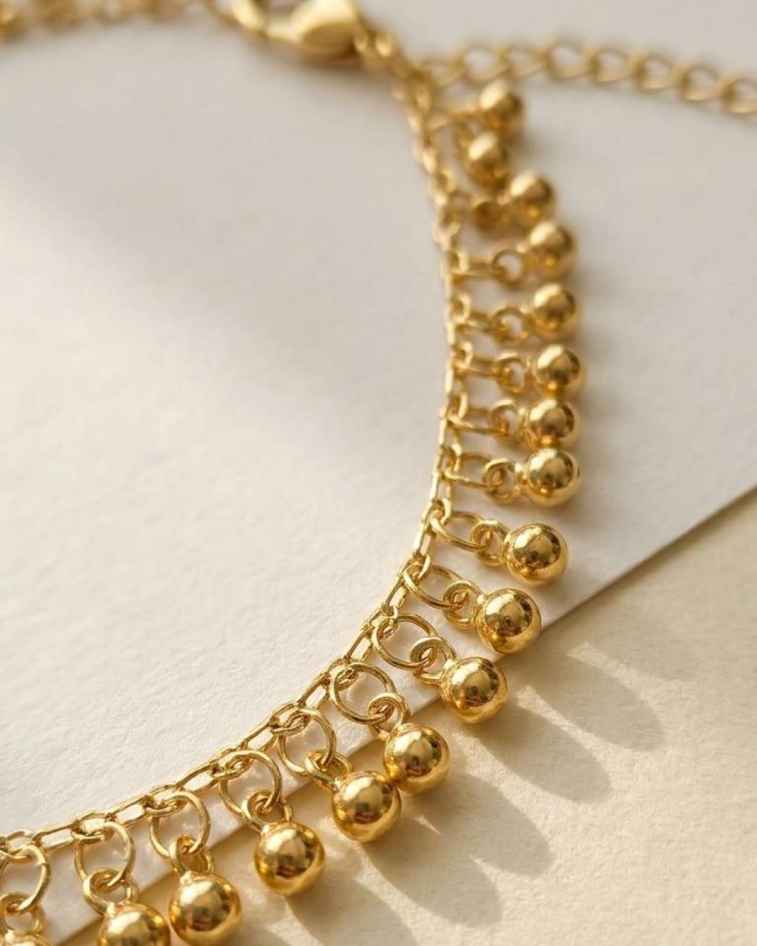 Macro detail of a gold anklet with tiny dangling sphere charms.