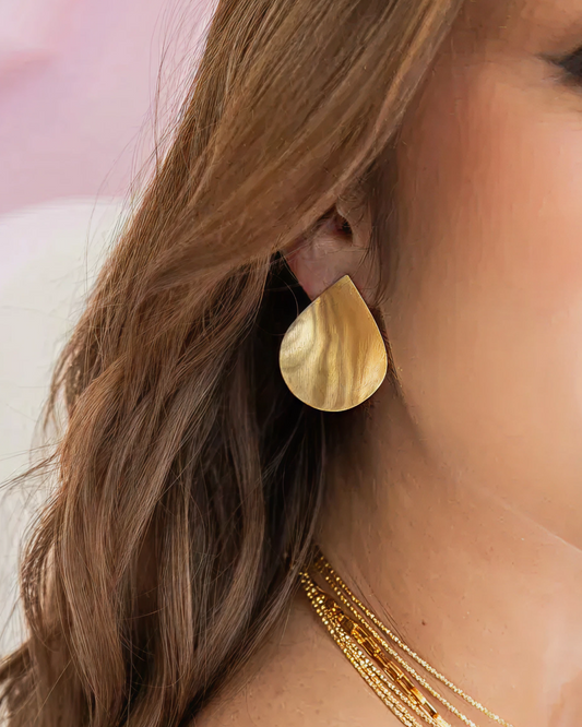 Close-up of satin gold teardrop earring on the earlobe.