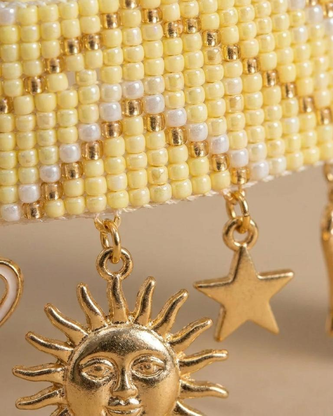 Macro detail of a yellow beaded bracelet with white and gold accents and gold-tone sun and star charms.