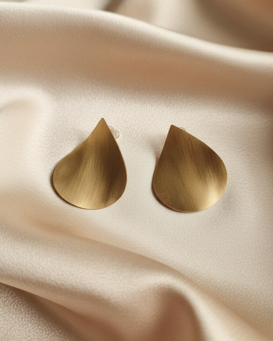 Brushed gold teardrop stud earrings displayed on champagne satin fabric.