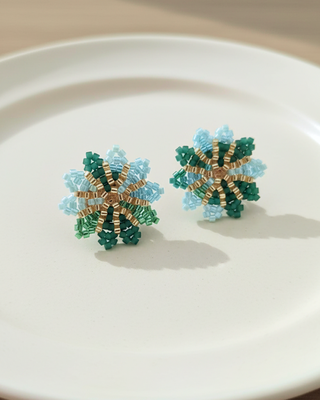 Miyuki beaded flower studs in aqua and green with gold center on a white plate.