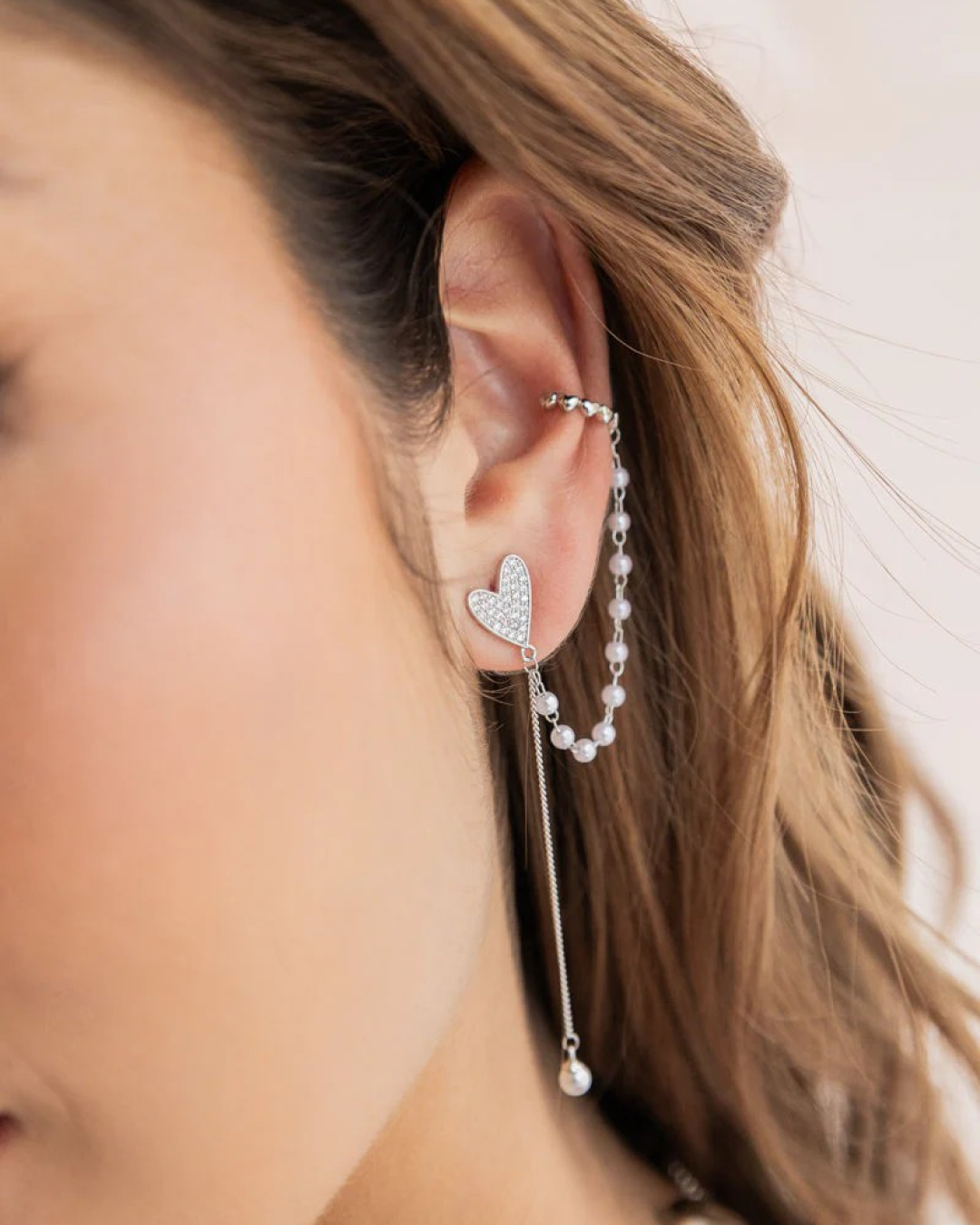 Silver-tone ear cuff with heart stud and double chain with pearls on the model’s ear, long drop.
