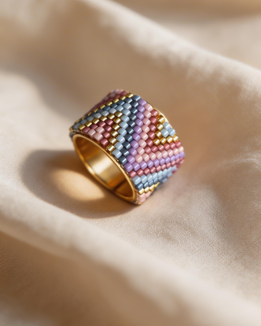 Wide Miyuki-woven ring with a chevron pattern in lilac, pink, blue, and gold on satin fabric.