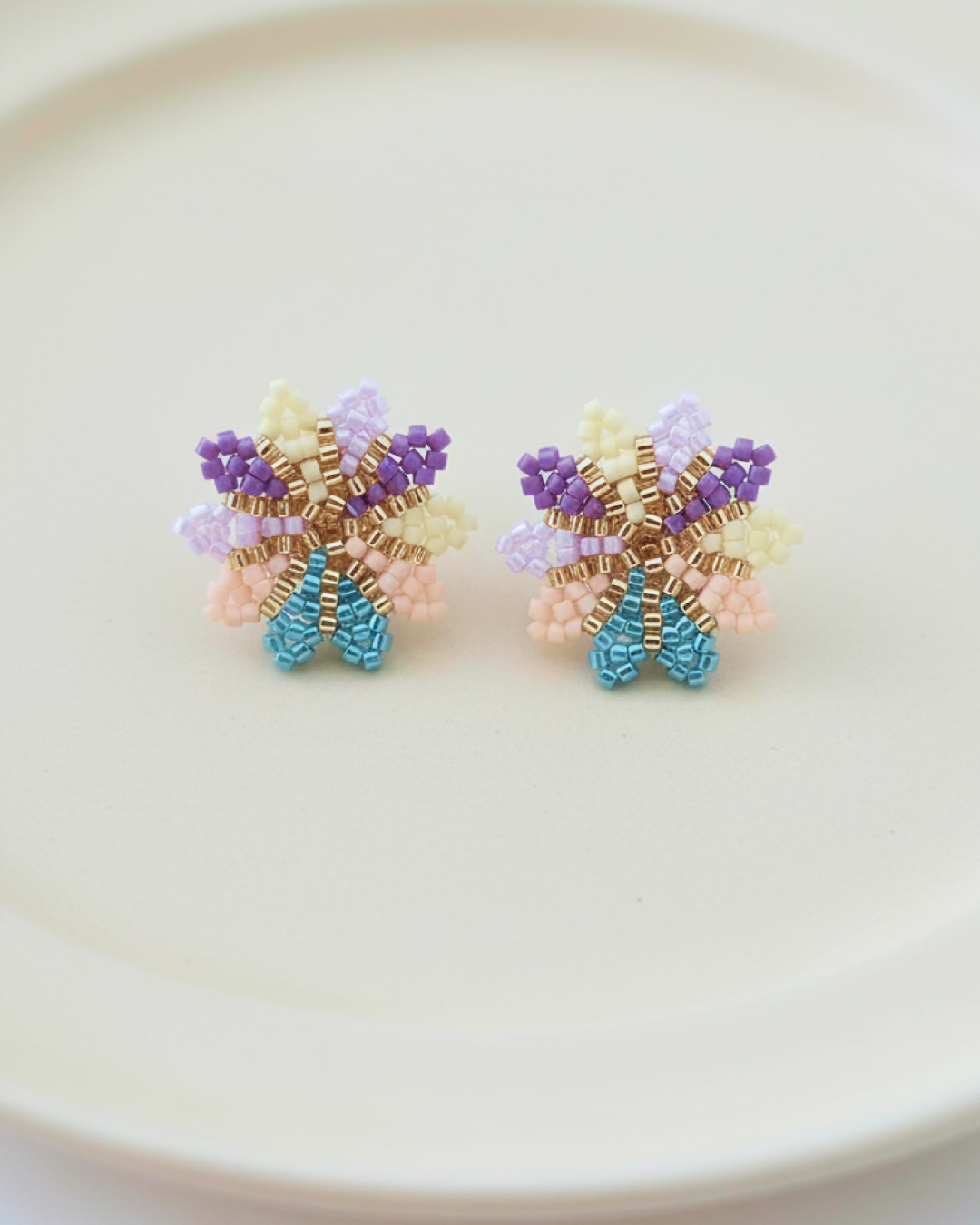 Miyuki beaded flower studs in pastel lilac with gold center on a beige plate.