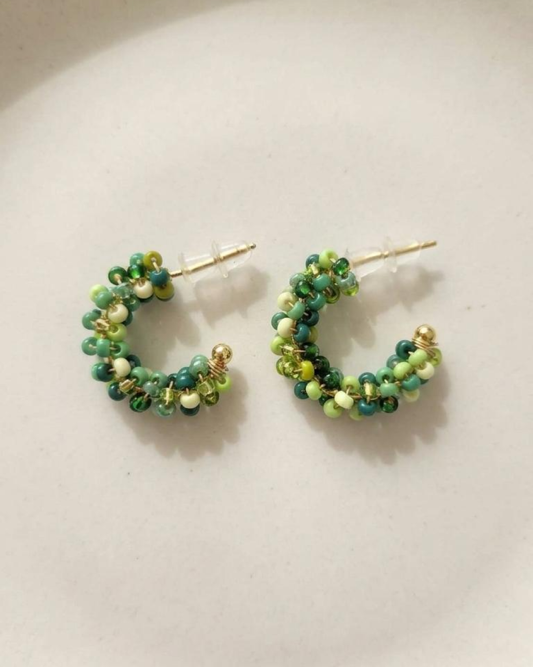 Pair of mini green beaded hoop earrings displayed on a neutral background.