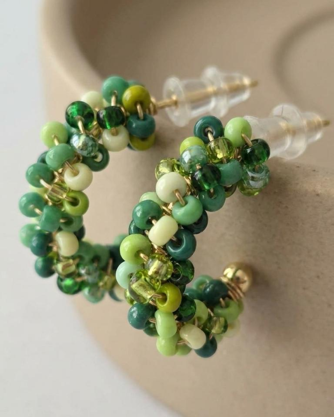 Macro detail of mini hoop earrings with green beads in mixed shades on a gold-tone base.