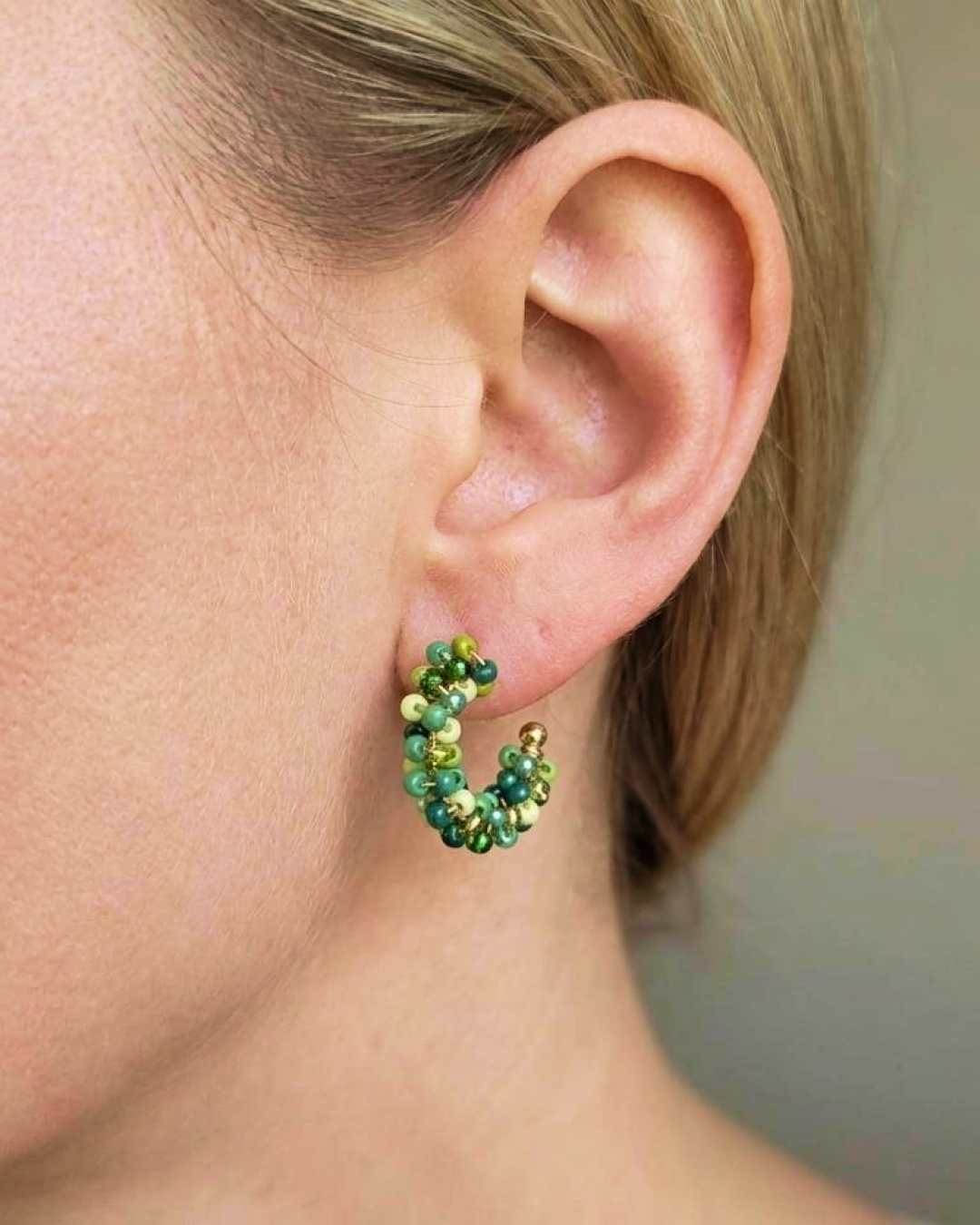 Close-up of a woman wearing mini green beaded hoop earrings with a gold-tone base.