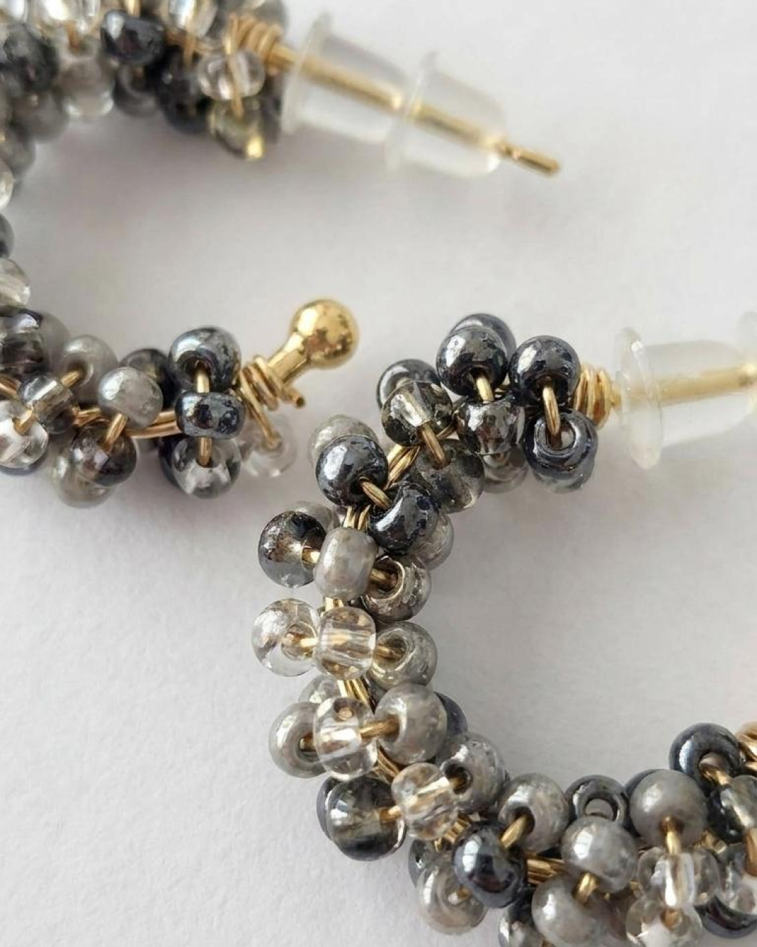 Macro close-up of grey and translucent beaded mini hoop earrings with a gold-tone base.
