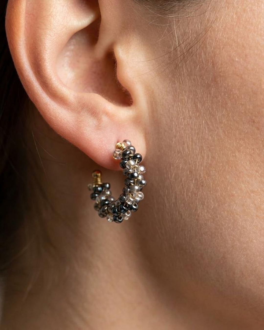 Close-up of a model wearing grey beaded mini hoop earrings with a gold-tone base.