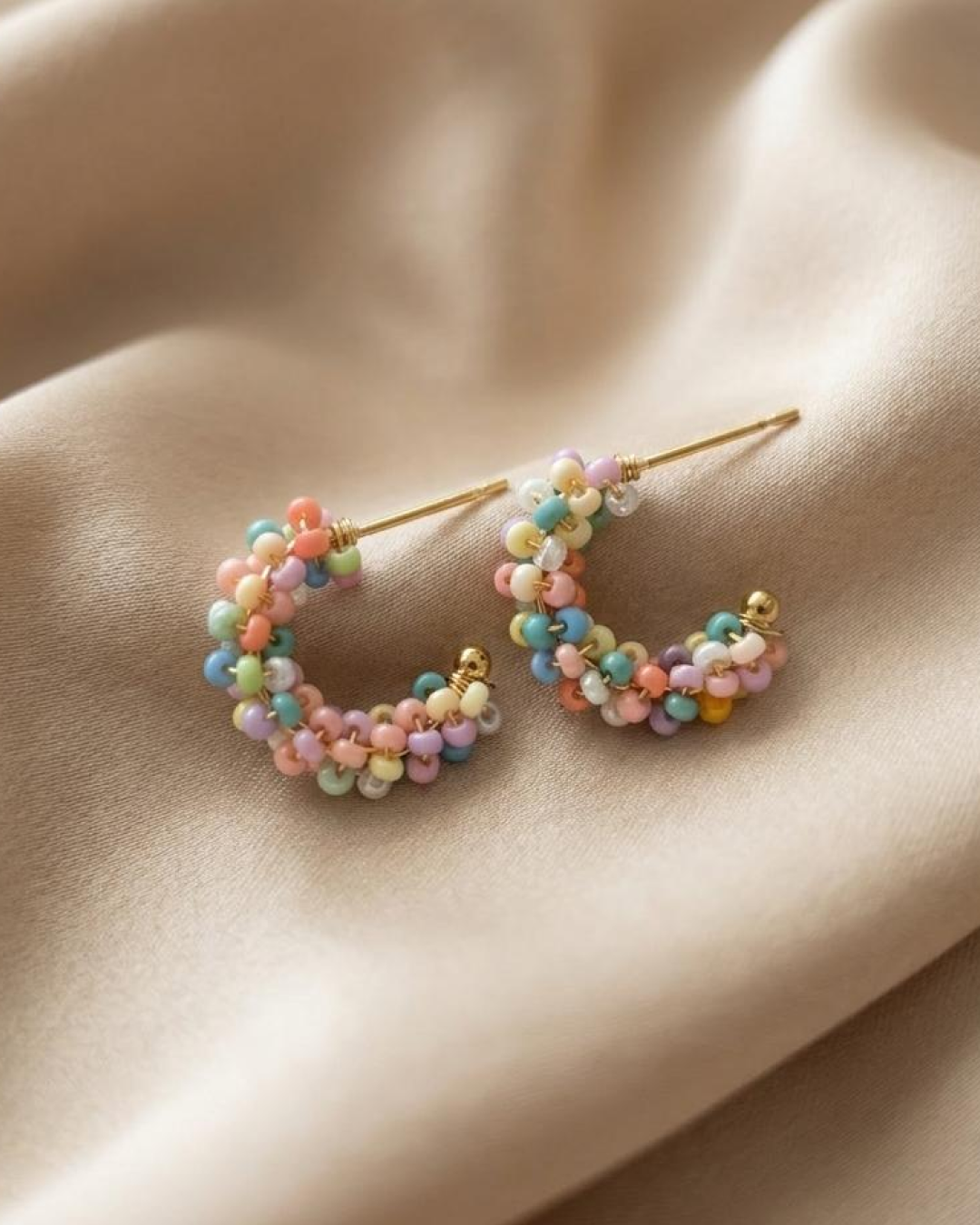 Pastel beaded mini hoop earrings displayed on champagne satin fabric with a gold-tone base.