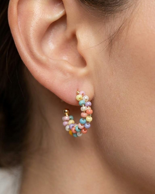 Close-up of a model wearing pastel beaded mini hoop earrings with soft pink, blue, yellow, and lilac tones.