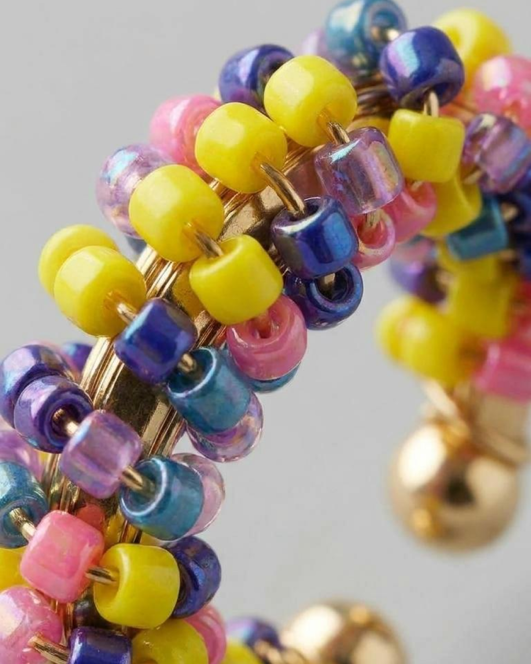 Macro close-up of a colorful beaded ear cuff with yellow, pink, blue, and purple beads on a gold-tone base.