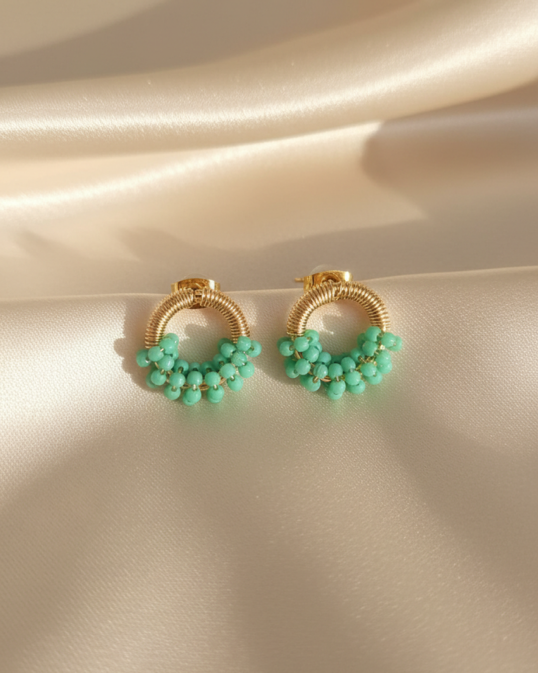 Pair of gold textured mini-ring stud earrings with mint murano-style clusters on satin fabric.