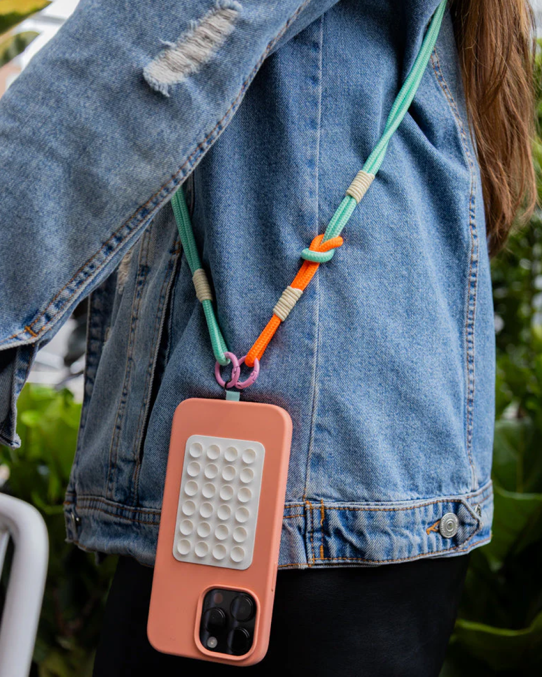 Model wearing a mint and orange phone strap with a coral phone case, styled over a denim jacket.