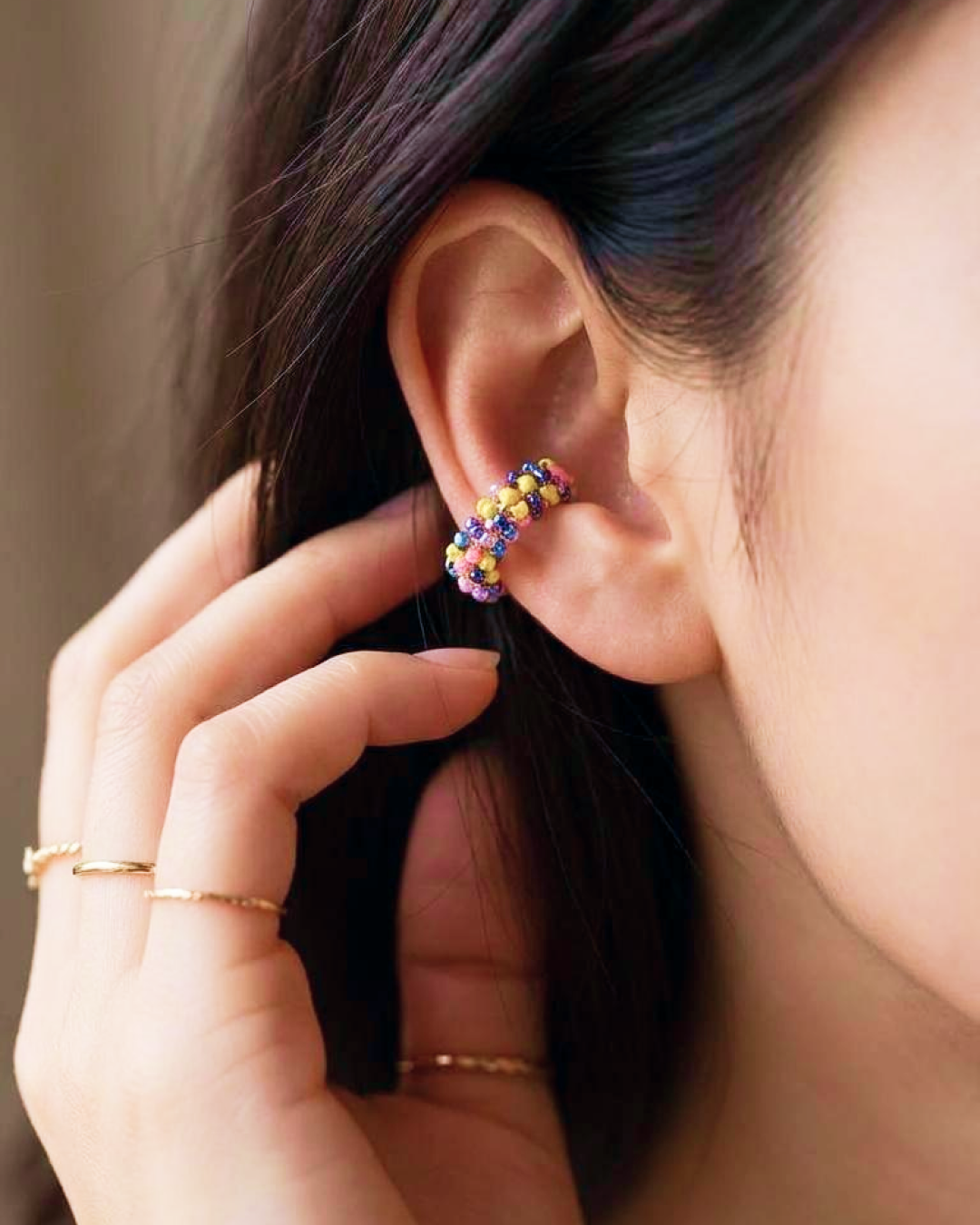 Close-up of a woman wearing a multicolor beaded ear cuff on the upper ear with delicate gold rings.