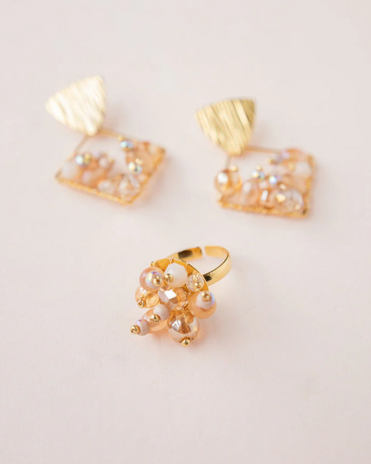 Adjustable gold ring with nude beaded cluster and glass pearls on a light background.