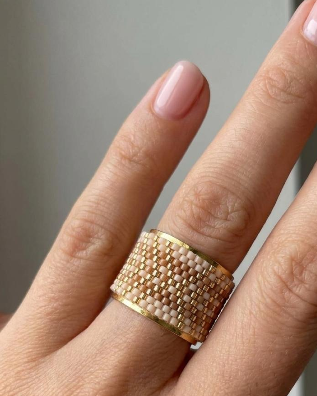 Close-up of a hand wearing a woven Miyuki ring in neutral and gold tones.