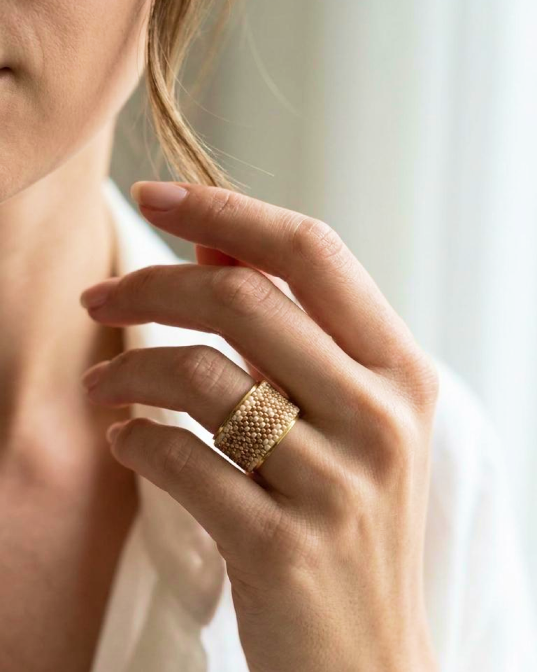 Hand wearing a wide-band nude Miyuki ring with a gold-tone base.